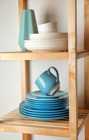 Shelving unit with set of dinnerware on light background. interior element