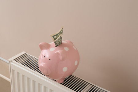 Heating radiator with piggy bank and money on color wallの写真素材