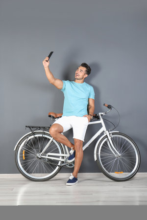 Handsome young hipster man taking selfie with bicycle near color wallの写真素材