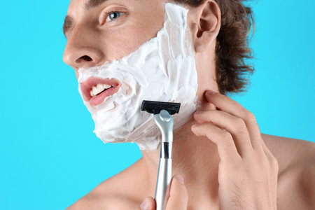 Handsome young man shaving on color backgroundの写真素材