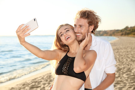 Happy young couple in beachwear taking selfie on seashoreの写真素材