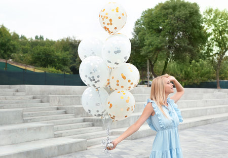 Beautiful young woman with bunch of balloons outdoorsの写真素材