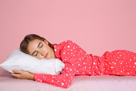 Beautiful teen girl sleeping with comfortable pillow on bed against color backgroundの写真素材