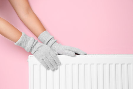 Woman in gloves warming hands on heating radiator near color wallの写真素材