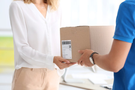 Young woman parcel receiving from courier in officeの写真素材