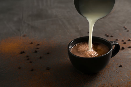Pouring milk into cup with tasty hot chocolate on table. Space for textの写真素材