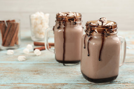 Jars of chocolate milk with marshmallows on light wooden table. Space for textの写真素材