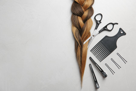 Flat lay composition with braid, hairdresser's tools and space for text on gray backgroundの写真素材