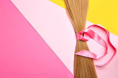 Blond hair tied with ribbon and space for text on color background, top viewの写真素材