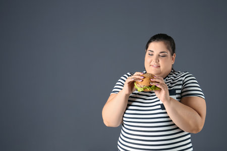 Overweight woman with hamburger and space for text on gray backgroundの写真素材