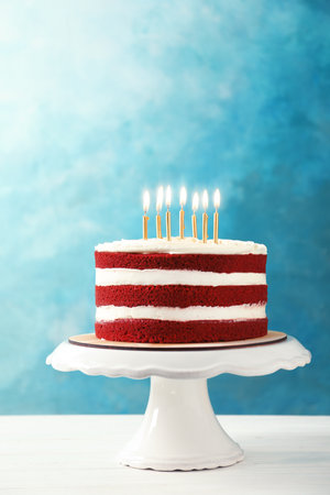 Delicious homemade red velvet cake with candles on table against color backgroundの写真素材