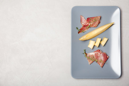 Plate of melon slices and prosciutto on gray background, top view. Space for textの写真素材