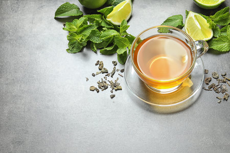 Cup with hot aromatic mint tea, lime, fresh and dry leaves on tableの写真素材