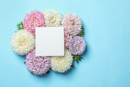 Beautiful aster flowers with sheet of paper on color background, top view. Space for textの写真素材