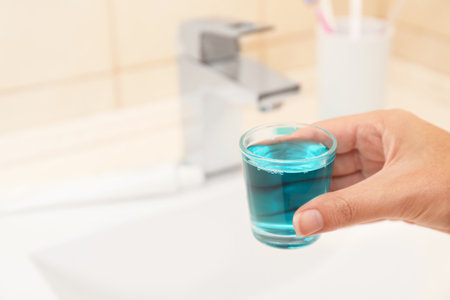 Woman holding glass with mouthwash for teeth and oral care in bathroomの写真素材