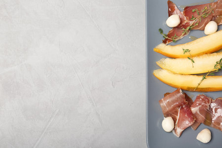 Plate of melon slices, mozzarella and prosciutto on gray background, top view. Space for textの写真素材