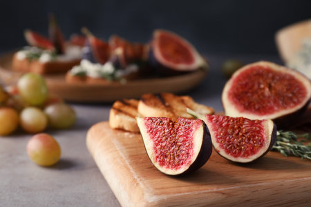 Wooden board with ripe fig slices on gray table, closeup