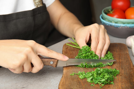 Woman cutting fresh green parsley on wooden board, closeupの写真素材