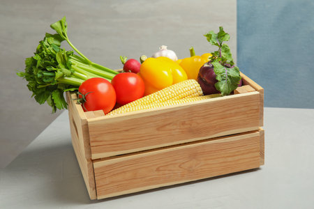 Wooden crate with fresh vegetables on gray table