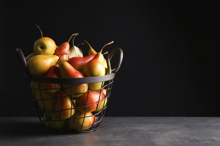 Basket with ripe pears on table against black background. Space for textの写真素材
