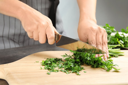 Woman cutting fresh green parsley on wooden board, closeupの写真素材