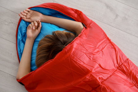 Young woman in comfortable sleeping bag on floor, top viewの写真素材