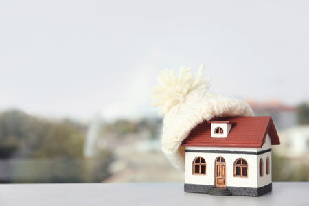 House model with knitted hat on table against blurred background, space for text. heating conceptの写真素材