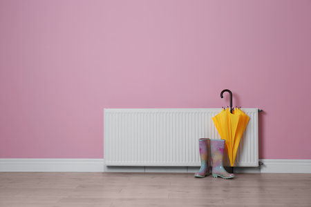 Modern radiator, rubber boots and umbrella near color wall with space for text. central heating systemの写真素材