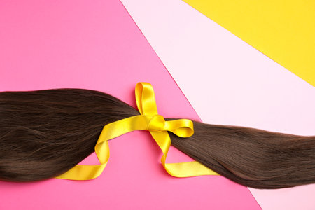 Brown hair tied with ribbon and space for text on color background, top viewの写真素材