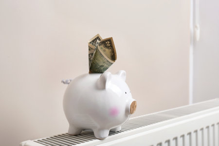 Piggy bank with money on heating radiator indoorsの写真素材