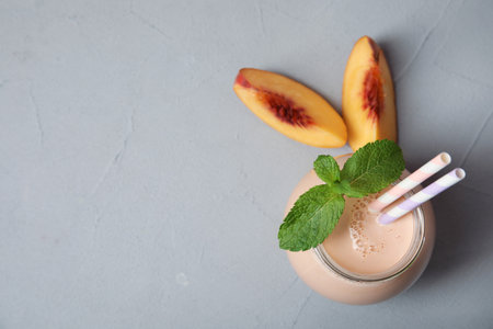 Jar of tasty milk shake with fresh peach and space for text on gray background, top viewの写真素材