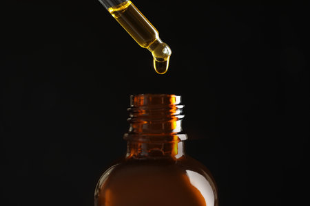 Pipette with oil over bottle on black backgroundの写真素材
