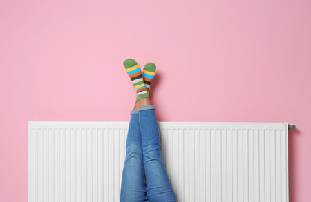 Woman warming legs on heating radiator near color wallの写真素材