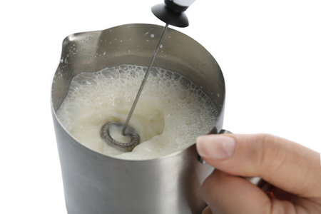 Woman using milk frother device in pitcher on white background, closeupの写真素材
