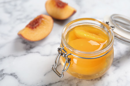 Glass jar with canned peach halves on marble background. Space for textの写真素材