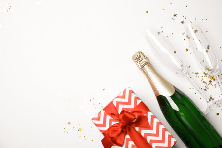 Creative flat lay composition with bottle of champagne, glasses and gift box on white background. Space for textの写真素材