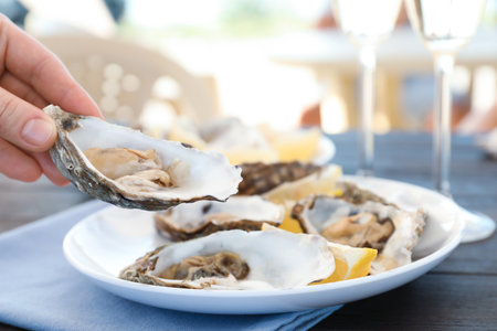 Woman with fresh oyster over plate, focus on handの写真素材