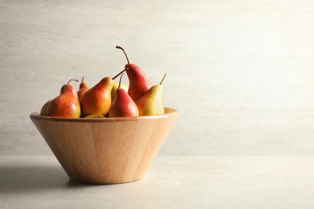 Bowl with ripe pears on table against light background. Space for textの写真素材