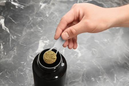 Man holding measuring spoon with hemp protein powder over jar on tableの写真素材