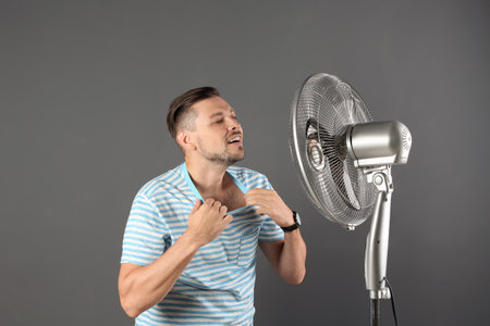 Man refreshing from heat in front of fan on gray backgroundの写真素材
