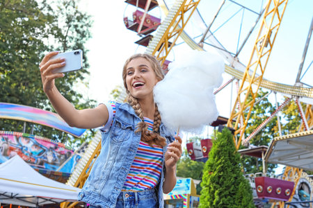 Attractive woman taking selfie with cotton candy in amusement parkの写真素材