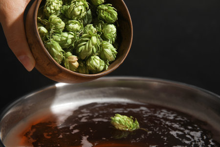 Woman adding fresh green hops to beer wort in pot, closeup