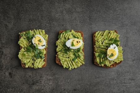 Tasty crisp rye toasts with avocado and quail egg on table, flat layの写真素材