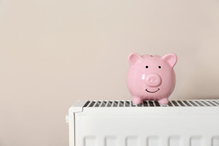 Piggy bank on heating radiator against light background. Space for textの写真素材