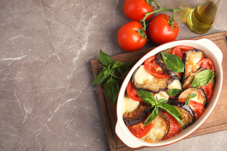 Flat lay composition with baked eggplant, tomatoes and basil in dishware on table. Space for textの写真素材