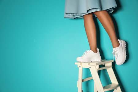 Woman in stylish sneakers on ladder near color wall, closeup. Space for text
