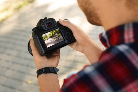 Male photographer holding professional camera with photo of benches on display in park, closeupの写真素材