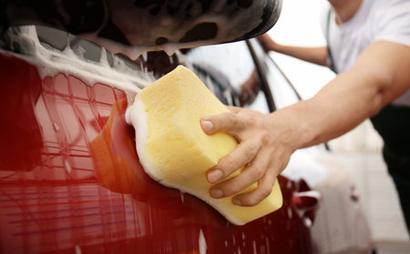 Male worker cleaning vehicle with sponge at car washの写真素材