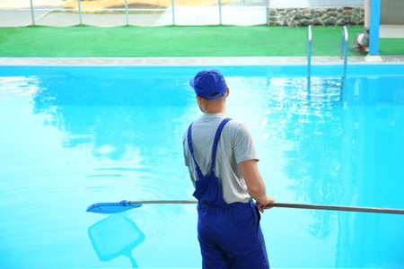 Male worker cleaning outdoor pool with scoop netの写真素材