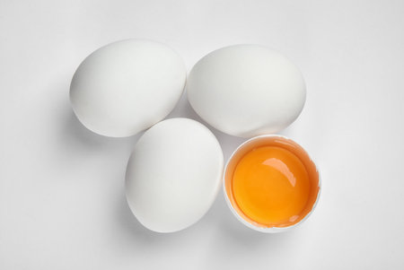 Cracked and whole chicken eggs on white background, top view